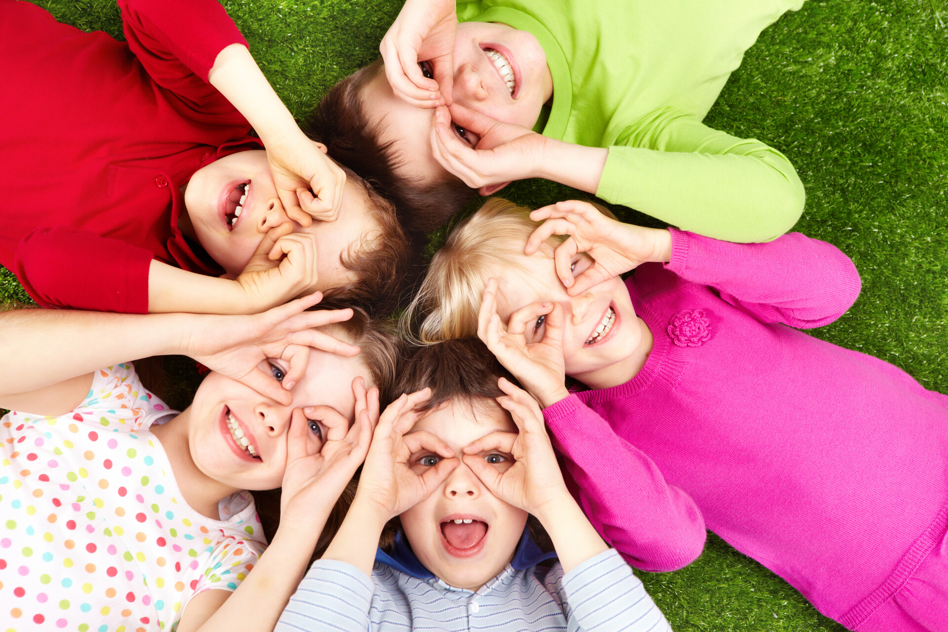 Kinder liegen auf dem Rücken im Kreis. Alle haben Daumen und Ringfinger zusammengetan und halten sie vor ihre Augen, wie eine Brille.