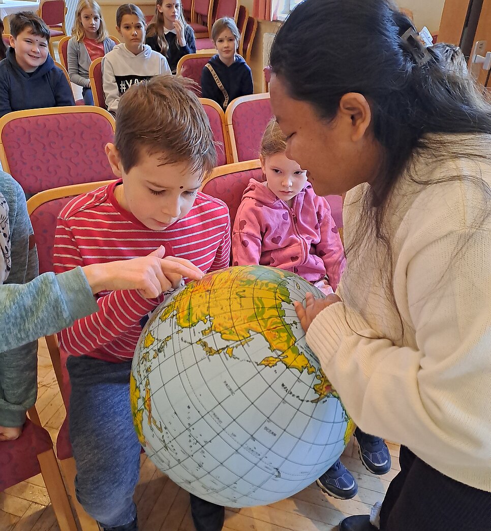 Projektpartnerin hält gemeinsam mit Kindern eine aufgeblasene Weltkugel.
