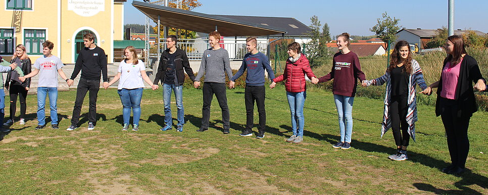 Credit: KJS St. Pölten Jugendliche stehen auf einer Wiese im Kreis und halten sich an den Händen.