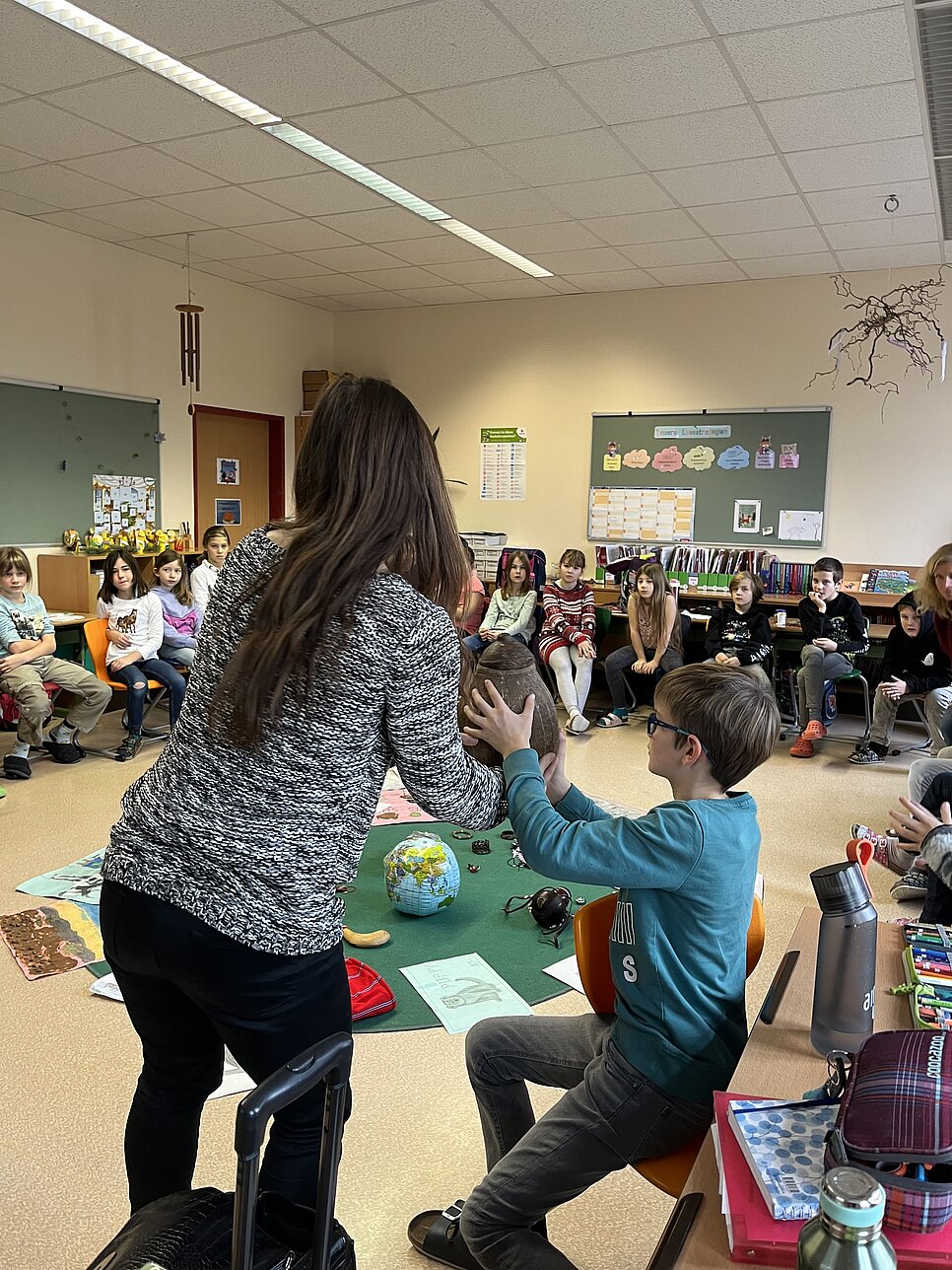 Sternsingen on tour Workshop mit einer Klasse. Die Referentin zeigt, den Kindern spezifische Gegenstände um das Projektland vorzustellen.